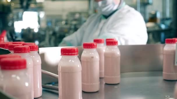Trabalhador da fábrica de produtos lácteos leva garrafas com iogurte de um transportador . — Vídeo de Stock