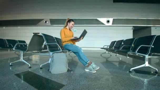 Uma mulher está sorrindo enquanto digita em um laptop no aeroporto — Vídeo de Stock