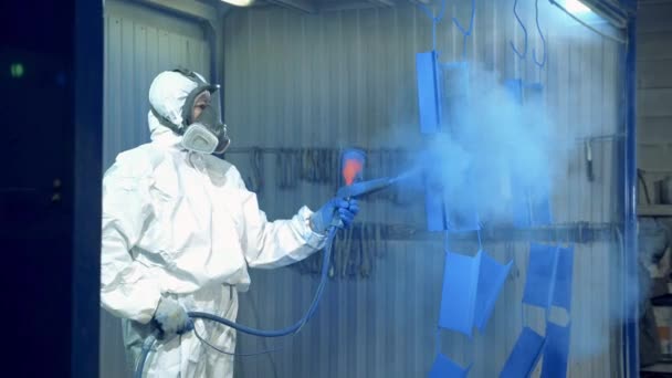 Een arbeider spuiten blauwe verf op metalen stukken in een schilderij fabriek faciliteit — Stockvideo