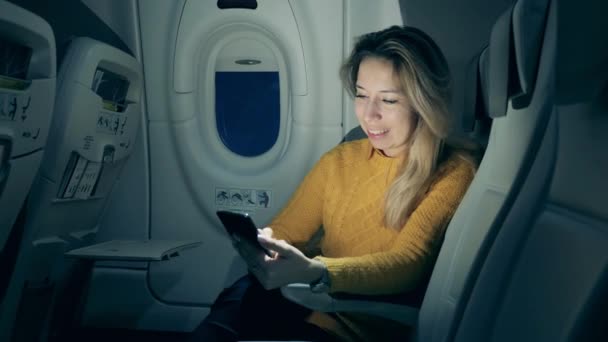 Uma senhora está sorrindo enquanto usa seu smartphone na cabine da aeronave — Vídeo de Stock