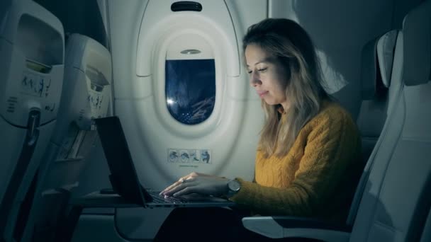 Hermosa mujer está escribiendo en una computadora portátil en la cabina del avión. Pasajera que trabaja dentro de un avión . — Vídeo de stock