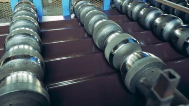 Rolling conveyor is processing metal shingles. Bending industrial equipment working with metal.