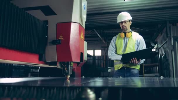 Un technicien masculin avec un ordinateur portable regarde une machine laser — Video