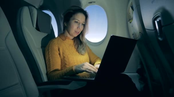 Airplane cabin and a woman typing on a laptop inside of it — 비디오