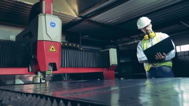 Fabrieksarbeider observeert een lasermechanisme op het werk — Stockvideo