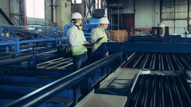 Two engineers are watching the conveyor with metal tile — Stock Video