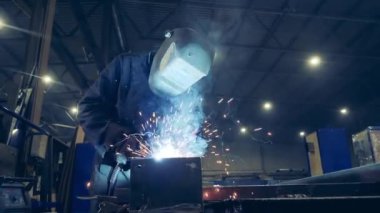 Worker in welders helmet is welding metal. Slow motion.