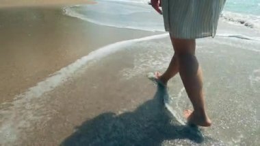 Female legs are shown while walking along the seaside