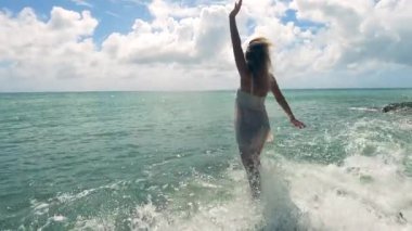 A lady is enjoying herself while standing on the rocks near the sea