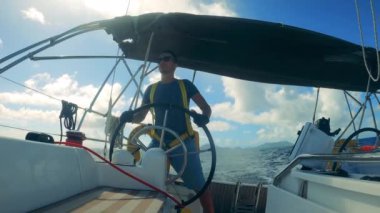 A man is standing at the wheel of a sailing boat