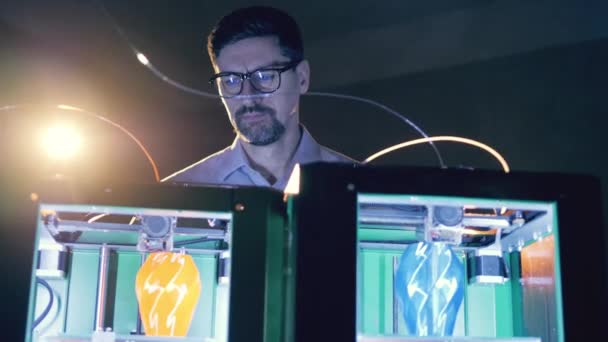 3Dプリント研究所で3Dプリンタで作業する男。専門家は3Dで花瓶を作る2台のプリンターを見ています — ストック動画