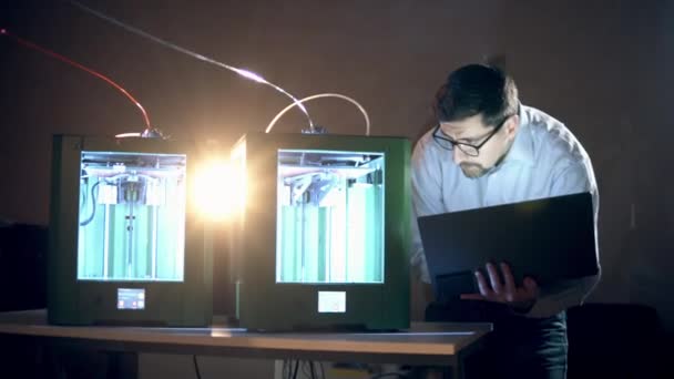 Técnico masculino com um laptop está inspecionando impressoras 3D — Vídeo de Stock