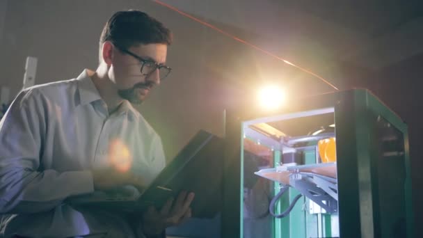La impresora 3D está siendo supervisada por un hombre con una computadora portátil — Vídeo de stock