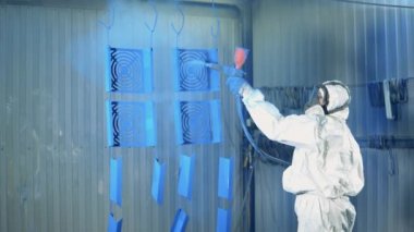 Mavi boya, bir kadın işçi tarafından metal plakalara püskürtülüyor. Boyama fabrikasında sanayi boyama işlemi.