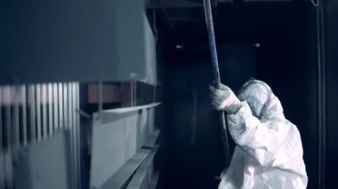 Female worker in safety wear is transporting metal plates into the industrial oven