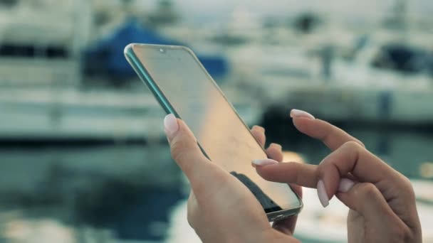 Close-up van vrouwen vingers typen op een smartphone naast water — Stockvideo