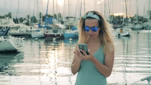 Πανέμορφη κυρία στο λιμάνι χαμογελάει ενώ πληκτρολογεί σε ένα τηλέφωνο — Αρχείο Βίντεο