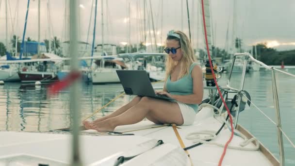 Hermosa dama sonríe mientras usa un ordenador portátil en un velero — Vídeos de Stock