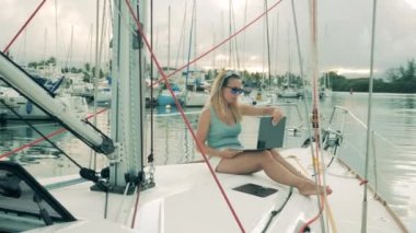 Yachts board with a woman browsing a laptop while sitting on it