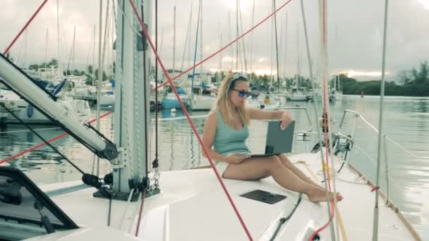 Yachts board with a woman browsing a laptop while sitting on it — Stockvideo