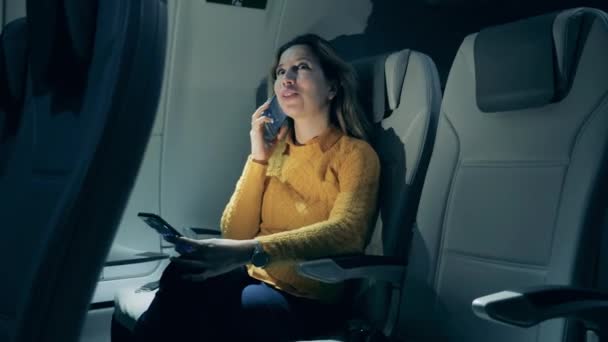 Egy nő beszél telefonon, miközben egy repülőgép kabinjában ül. — Stock videók