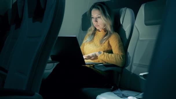 A woman is working on a laptop during her night flight. Female freelancer working on laptop sitting In airplane. — Stock Video