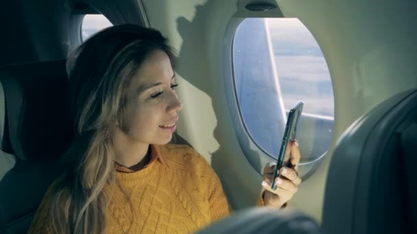 Smiling lady is browsing her phone during the plane flight — 비디오