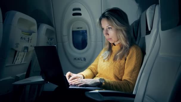 Female freelancer working on laptop sitting In airplane. A lady is working on a laptop in semi-darkness while being on a plane — Stock Video