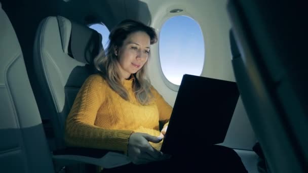 Schöne Frau arbeitet an einem Laptop im Flugzeug bei Sonnenaufgang — Stockvideo