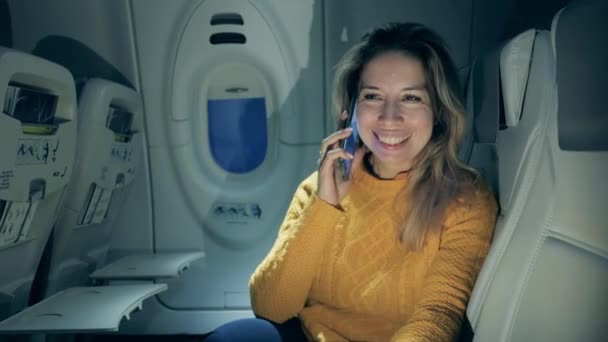 Mulher bonita está sendo feliz ao falar ao telefone em um avião — Vídeo de Stock