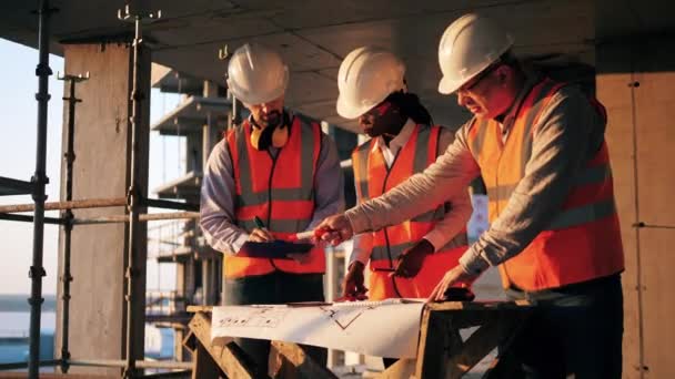 Three engineers work with a blueprint in a building. Construction contractor working on a construction site. — Stock video