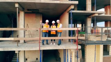 Çok ırklı mühendisler, mimarlar inşaat planını tartışıyor. İnşaatçılar inşaat alanındaki evleri kontrol ediyorlar..