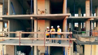 Mühendisler inşaat alanında çalışıyor, belgeleri kontrol ediyorlar. Çok ırklı mühendisler, mimarlar inşaat planını tartışıyor.