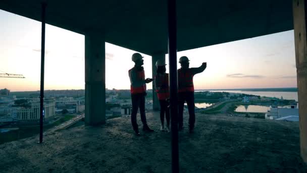 Des hommes et une femme debout dans un bâtiment, discutant du chantier . — Video