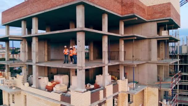 Tres trabajadores de la construcción hablan mientras están de pie en un sitio. Ingenieros multiétnicos, arquitectos discutiendo plan de construcción . — Vídeo de stock
