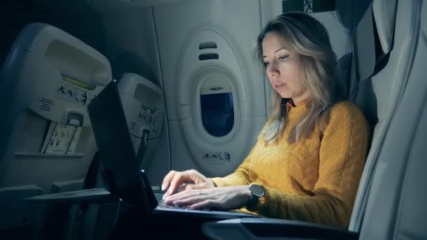 Cabina de avión en semi-oscuridad con una mujer escribiendo en un ordenador portátil — Vídeos de Stock