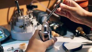 A goldsmith in jewelry working with ring. Working jeweller puts yellow gemstone on a ring.