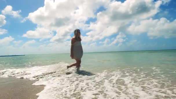 Солнечный берег и веселая женщина, идущая вдоль него — стоковое видео