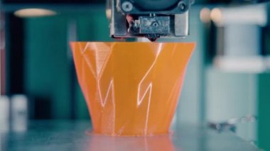 3D-printing machine is producing an orange vase. Three dimensional 3d printer working at 3d printing lab.