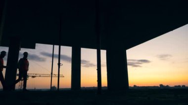 Professional engineers work in unfinished house on a sunset background.