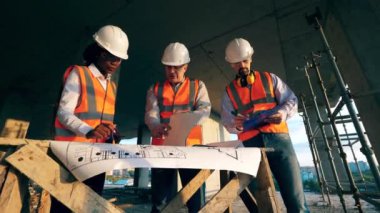 Multiethnic engineers, architects discussing construction plan. Engineers work with a blueprint on a table on a construction site.