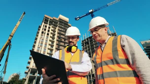 Робочі інженери, будівельники обговорюють план будівництва з використанням ноутбука, стоячи на будівельному майданчику . — стокове відео