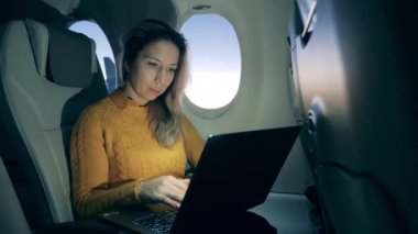 Aircraft cabin with a lady working on a laptop during her flight