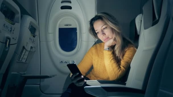 Beautiful lady is browsing her phone during a night flight — Stockvideo