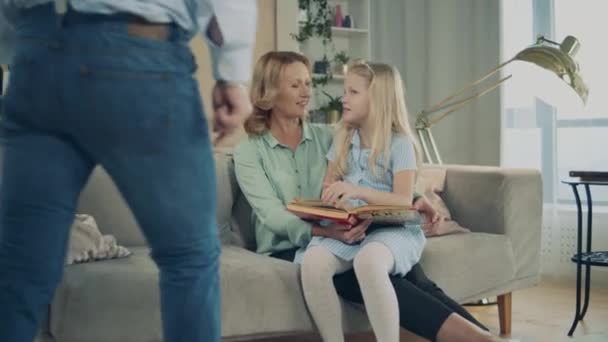 Living room with a little girl reading with her grandparents — Stockvideo