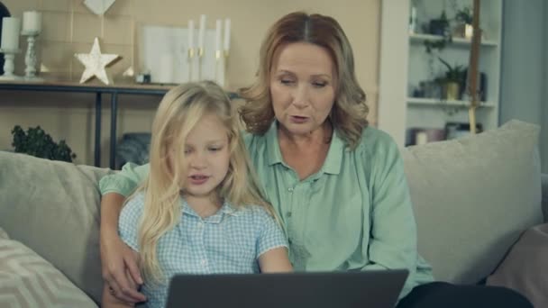 Маленькая девочка и ее бабушка смеются перед ноутбуком — стоковое видео