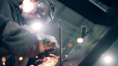 Man uses a grinding machine while working at a factory. Lots of grinding sparks.