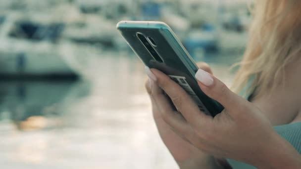 Een vrouw werkt met een smartphone terwijl ze in een haven staat. — Stockvideo