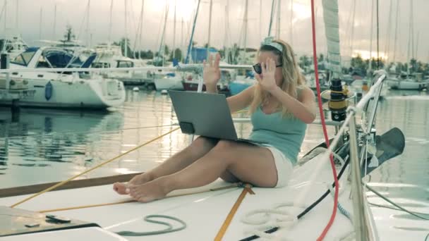 Mujer joven se comunica a través de un ordenador portátil mientras está sentado en un yate. Video chat, concepto de videollamada . — Vídeos de Stock