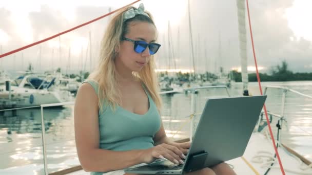 Young woman types on a laptop while working at yacht. — Stock Video